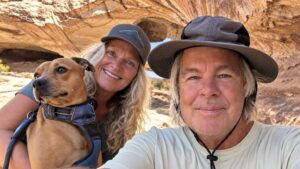 Mel and Eben smiling with their dog Bodie in front of sandstone rock formations during their travels.